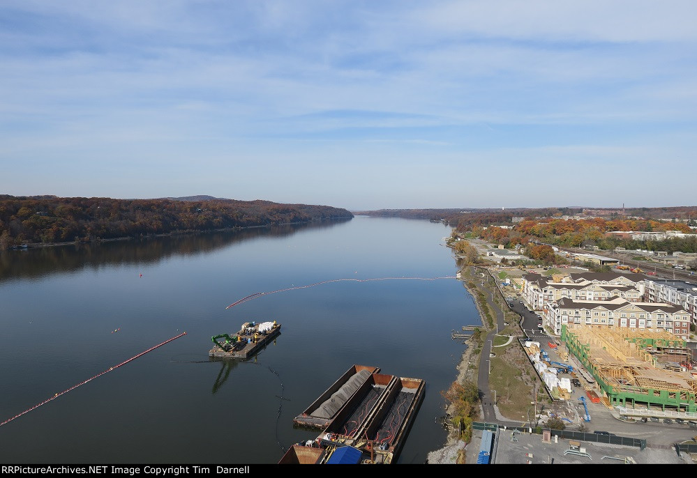 Looking north at a barge, railroads on either side of the river.